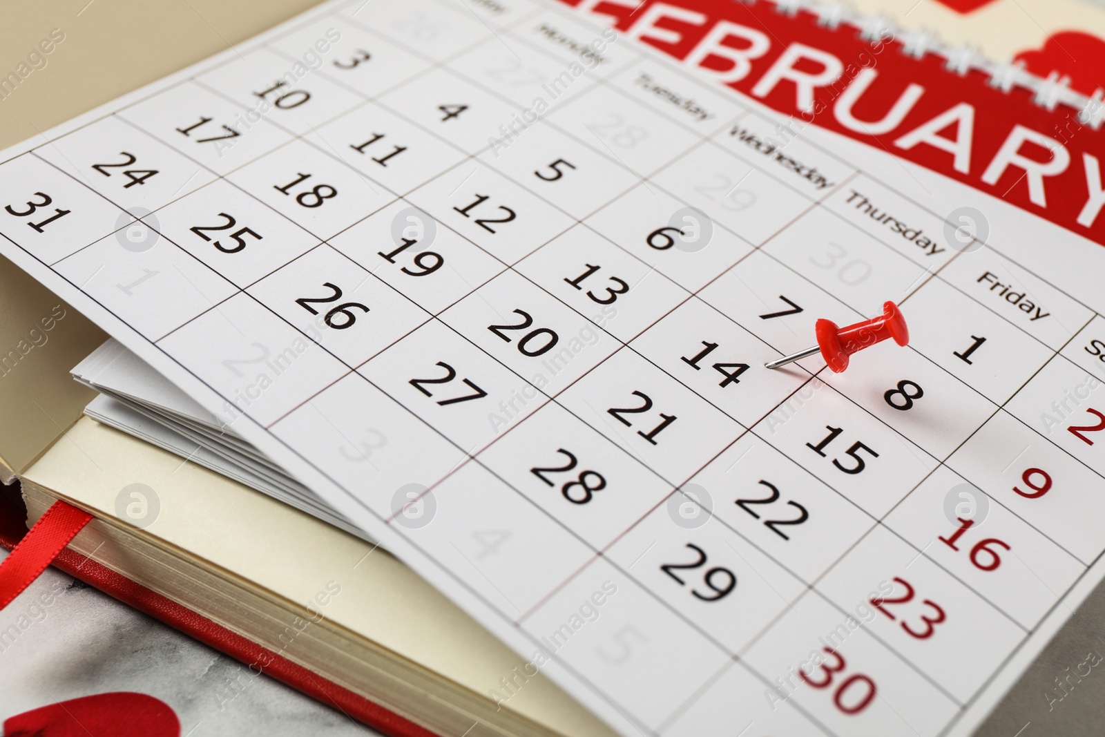 Photo of Calendar with marked Valentine's Day and notebooks on white marble table, closeup