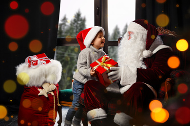 Santa Claus giving Christmas gift to little boy near window indoors