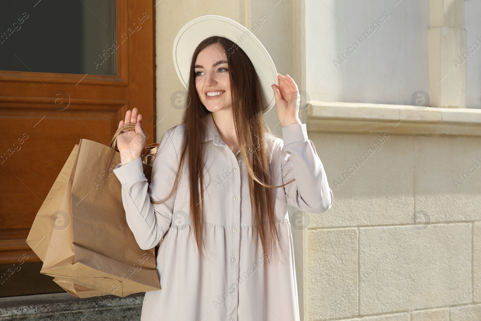 Photo of Beautiful young woman with shopping bags near building outdoors