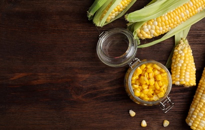 Photo of Tasty sweet corn kernels in jar and fresh cobs on wooden table, flat lay. Space for text