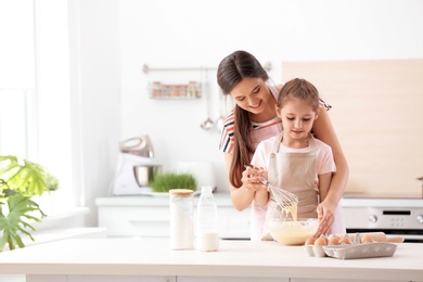 Photo of Mother and her daughter making dough at table in kitchen