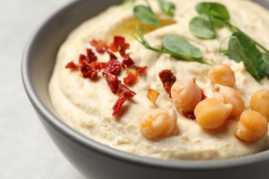 Photo of Tasty hummus with garnish in bowl on grey background, closeup