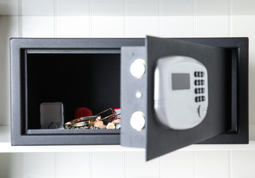 Photo of Open black steel safe with money and jewelry on shelf