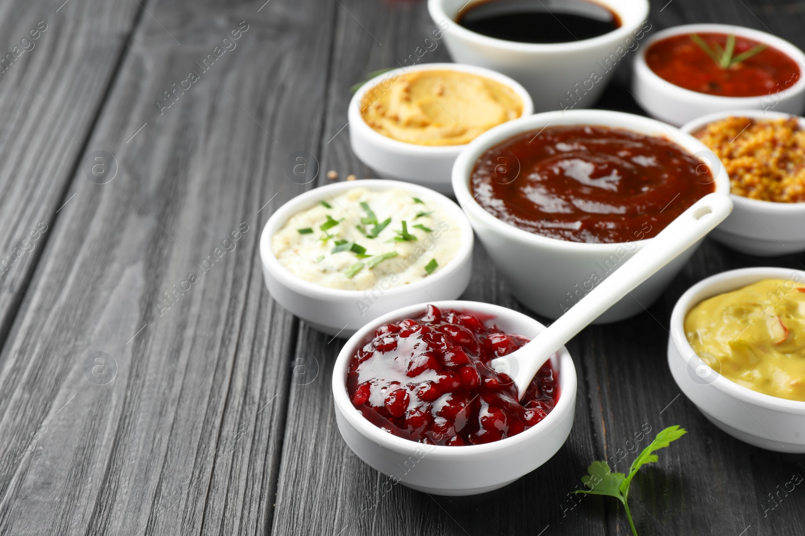 Photo of Different tasty sauces in bowls and parsley on black wooden table, closeup. Space for text