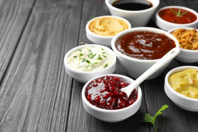 Photo of Different tasty sauces in bowls and parsley on black wooden table, closeup. Space for text