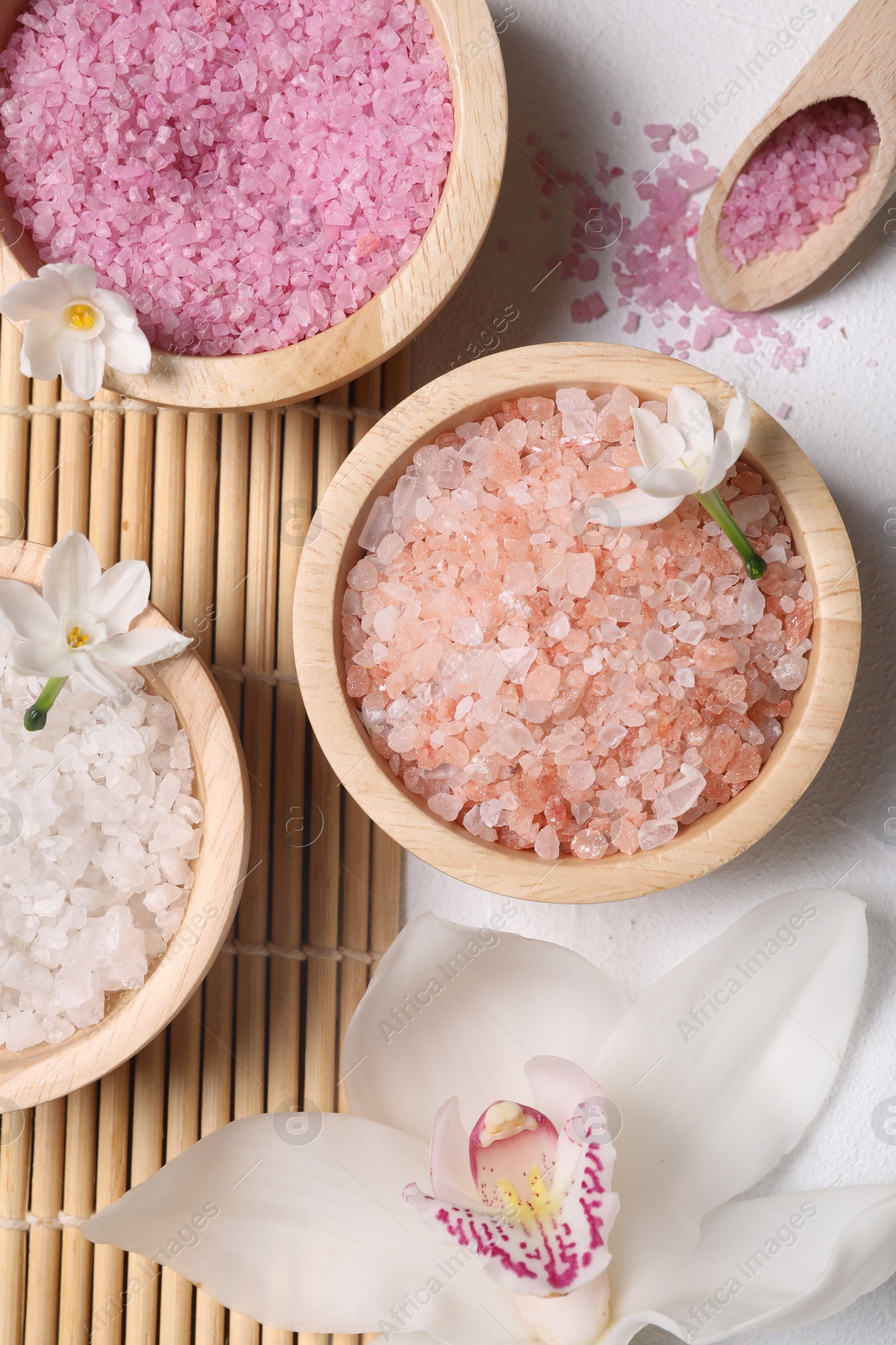 Photo of Different types of sea salt and flowers on light table, flat lay. Spa products