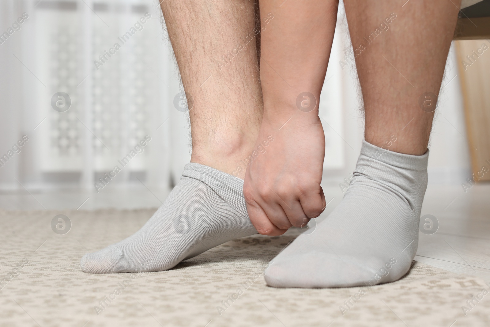 Photo of Man putting on light socks at home, closeup