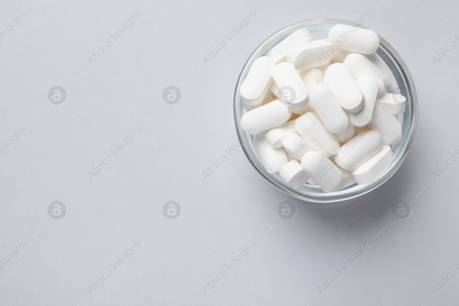 Photo of Vitamin capsules in bowl on light grey background, top view. Space for text