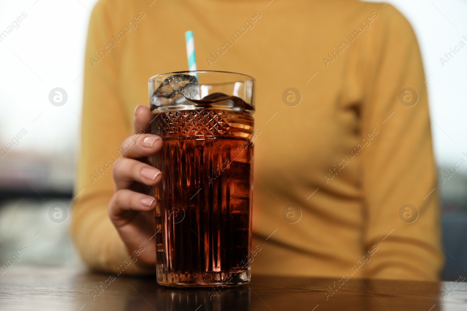 Photo of Woman with glass of refreshing cola at table indoors, closeup. Space for text