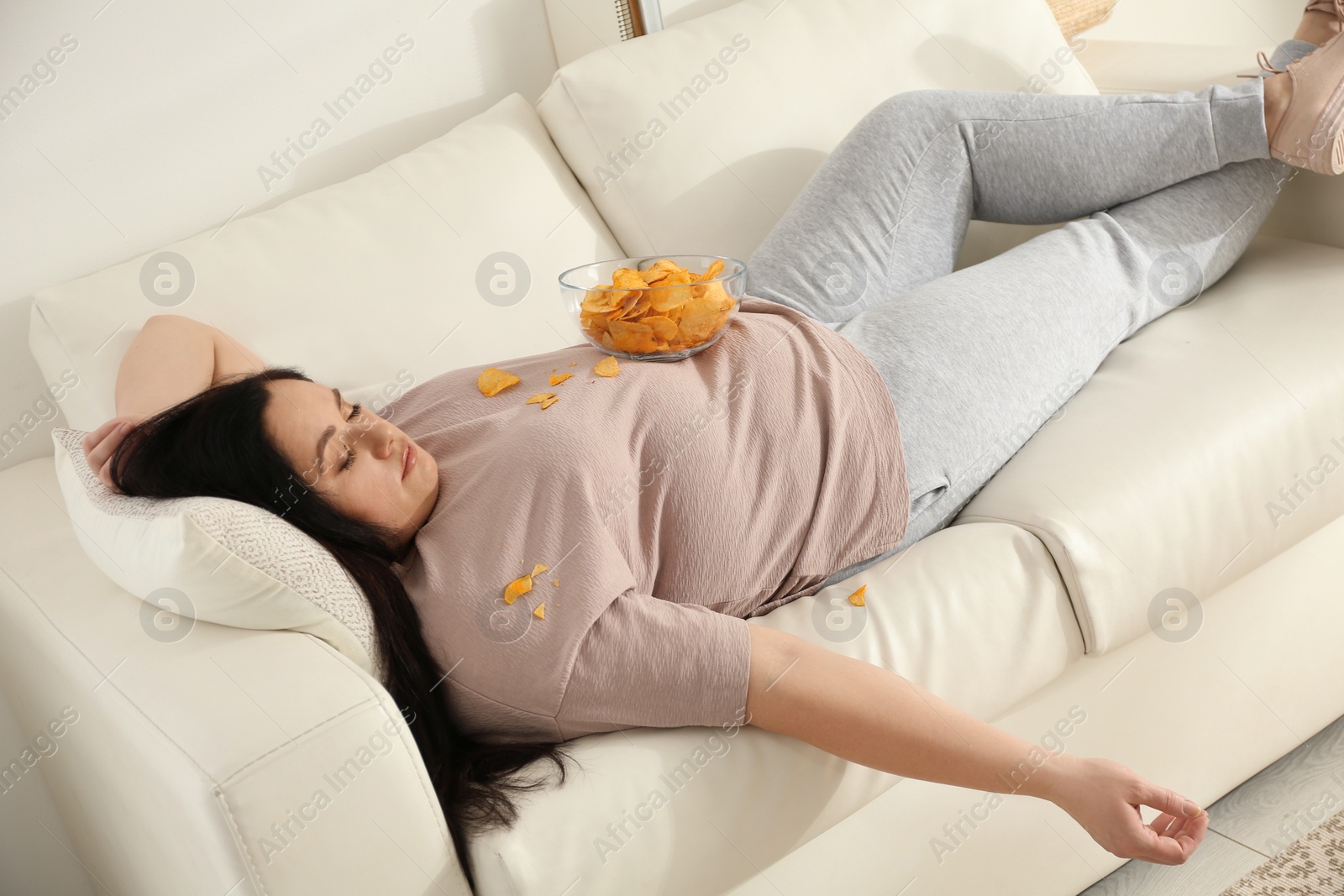 Photo of Lazy overweight woman with chips resting on sofa at home