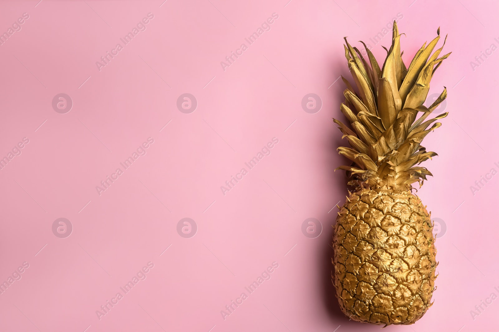 Photo of Top view of painted golden pineapple on pink background, space for text. Creative concept