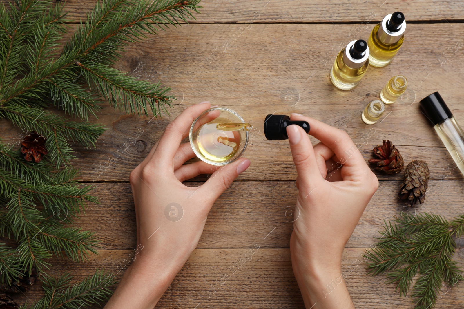 Photo of Woman holding bowl with pine essential oil at wooden table, top view