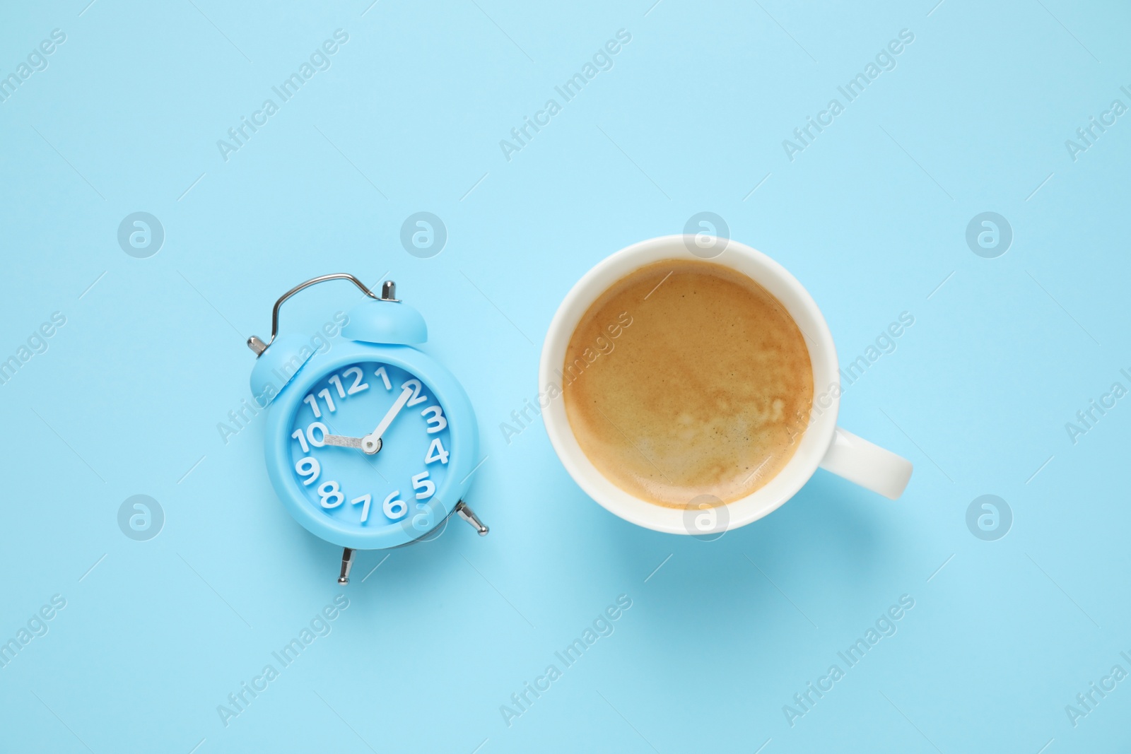 Photo of Cup of morning coffee and alarm clock on light blue background, flat lay
