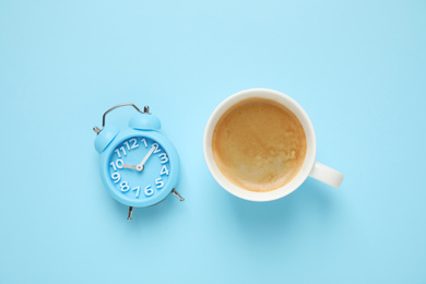 Photo of Cup of morning coffee and alarm clock on light blue background, flat lay