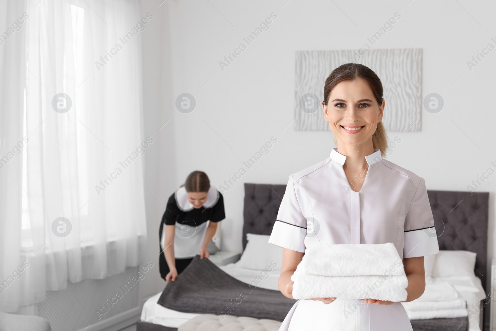 Photo of Professional chambermaid holding pile of clean towels in bedroom