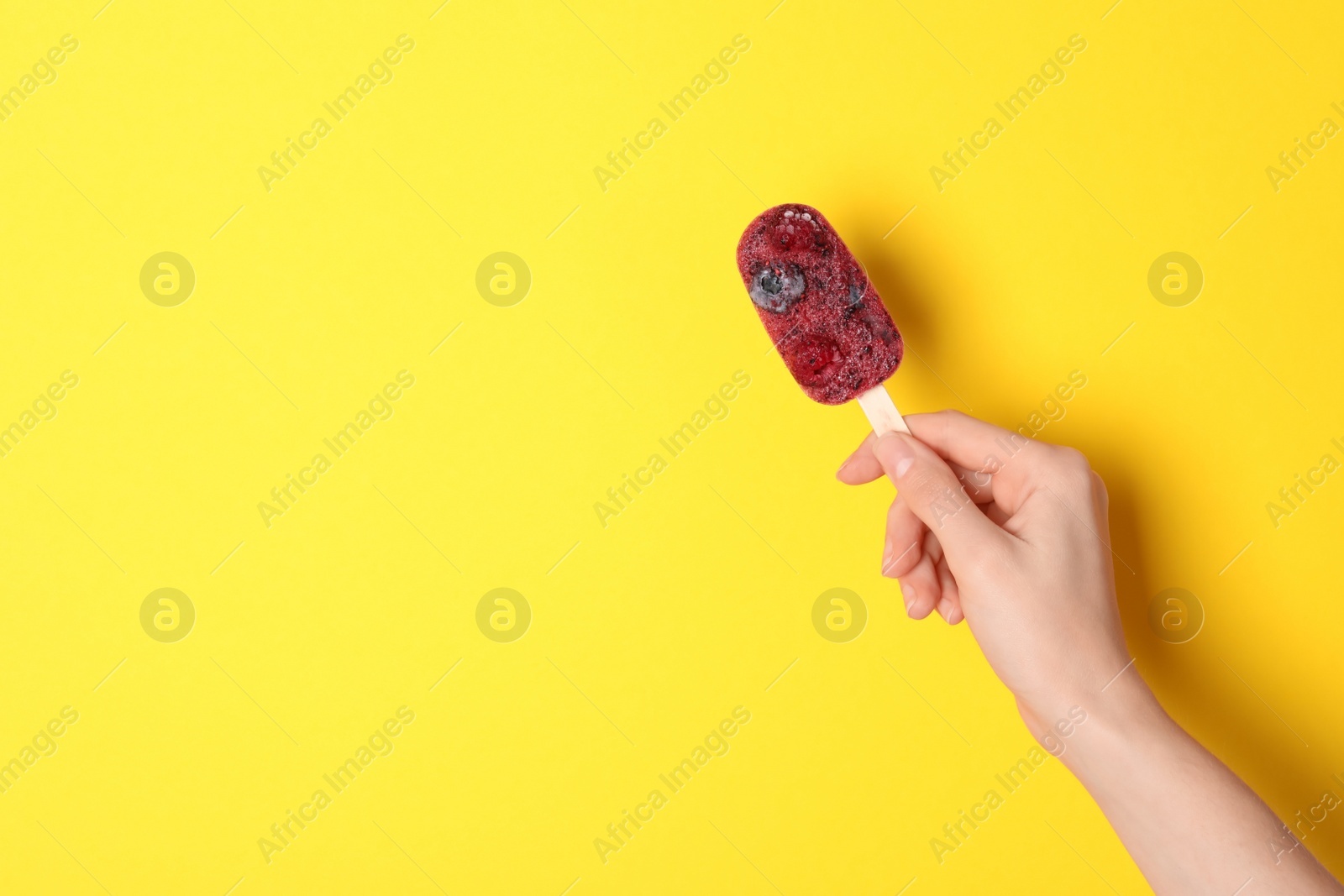 Photo of Woman holding tasty fruit ice pop on yellow background, space for text