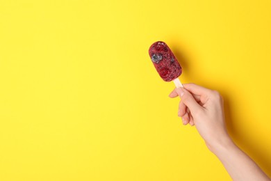 Photo of Woman holding tasty fruit ice pop on yellow background, space for text