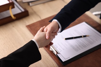 Photo of Notary shaking hands with client at wooden table, closeup