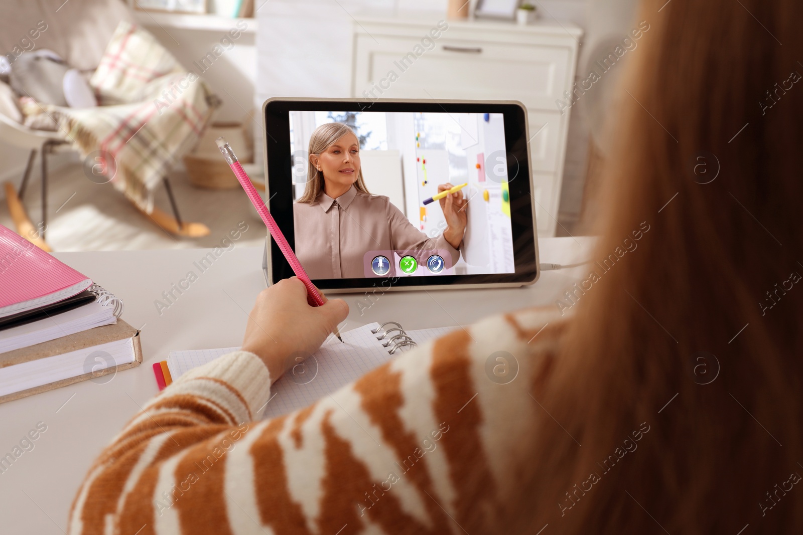 Image of E-learning. Little girl taking notes during online lesson at table indoors, closeup