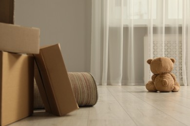 Photo of Cute lonely teddy bear on floor near boxes indoors, back view
