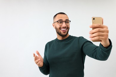 Smiling young man taking selfie with smartphone on grey background, space for text