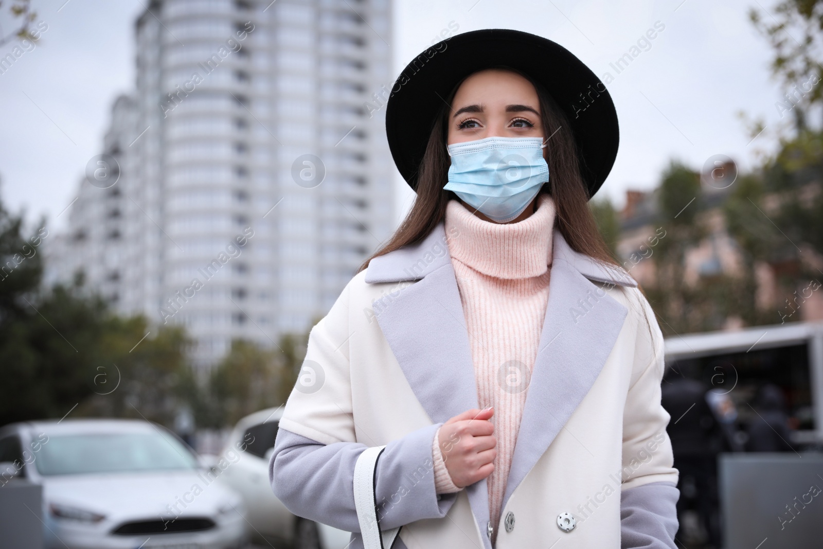 Photo of Young woman in medical face mask walking outdoors. Personal protection during COVID-19 pandemic