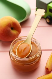 Photo of Spoon with healthy baby food and glass jar on pink wooden table, closeup