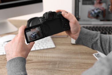 Professional photographer with digital camera at wooden table indoors, closeup