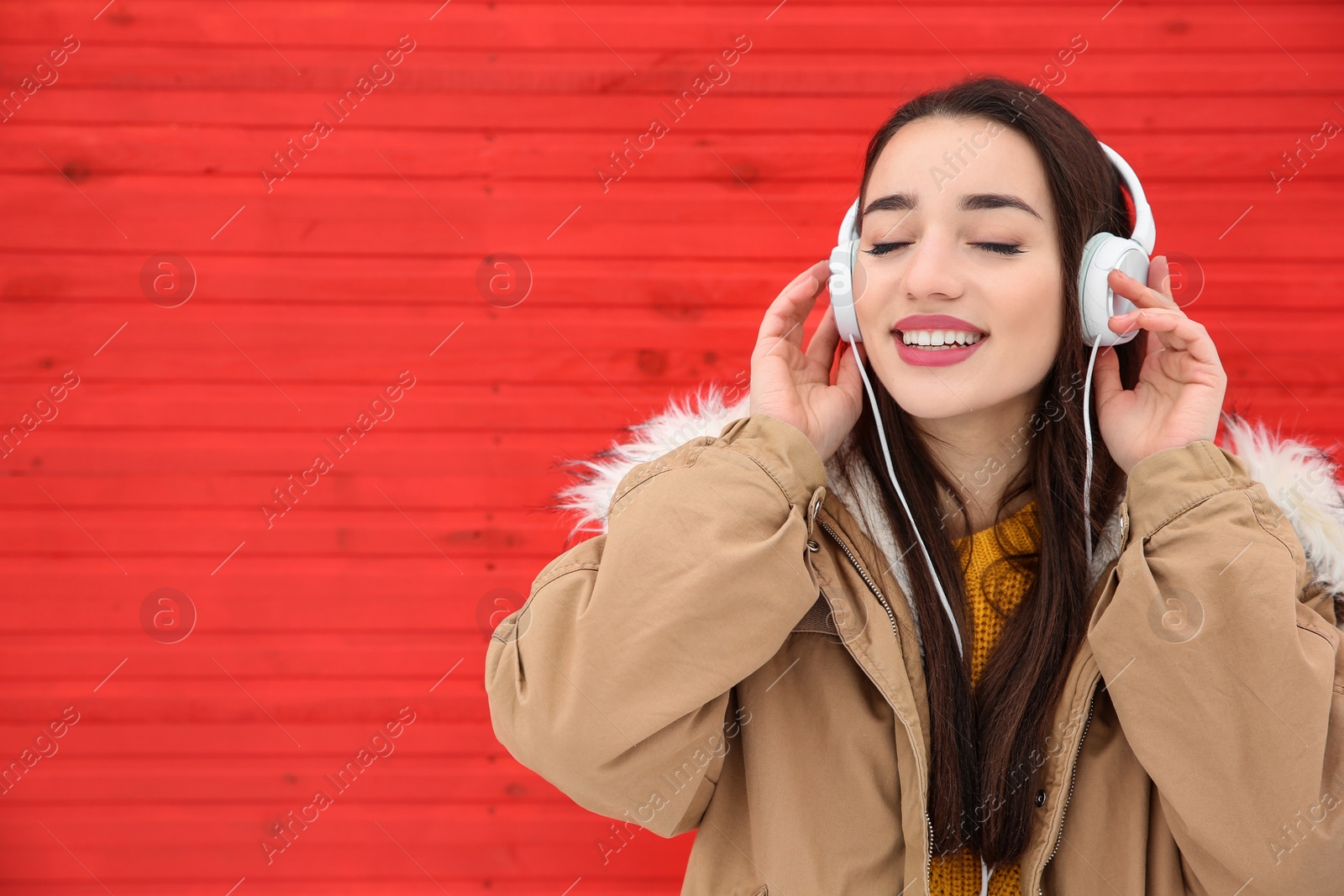 Photo of Beautiful young woman listening to music with headphones against color wall. Space for text