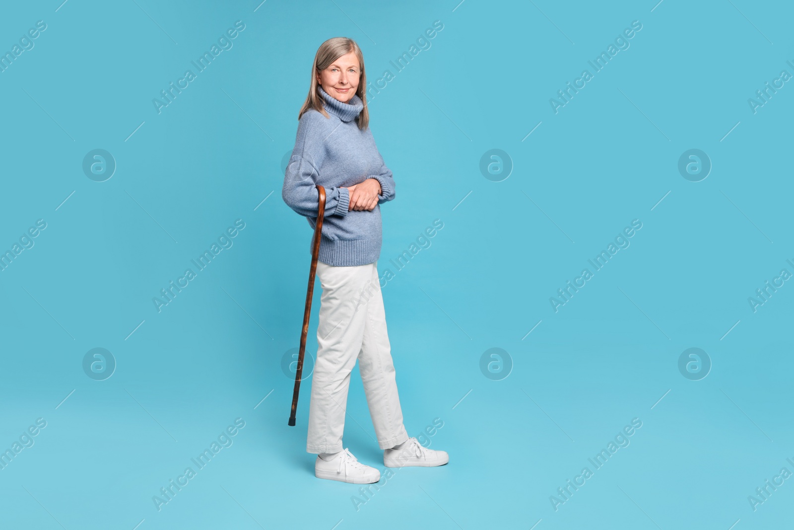 Photo of Senior woman with walking cane on light blue background