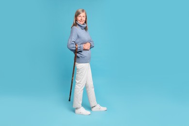 Senior woman with walking cane on light blue background