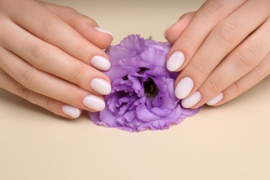 Photo of Woman with white nail polish holding violet eustoma flower on beige background, closeup