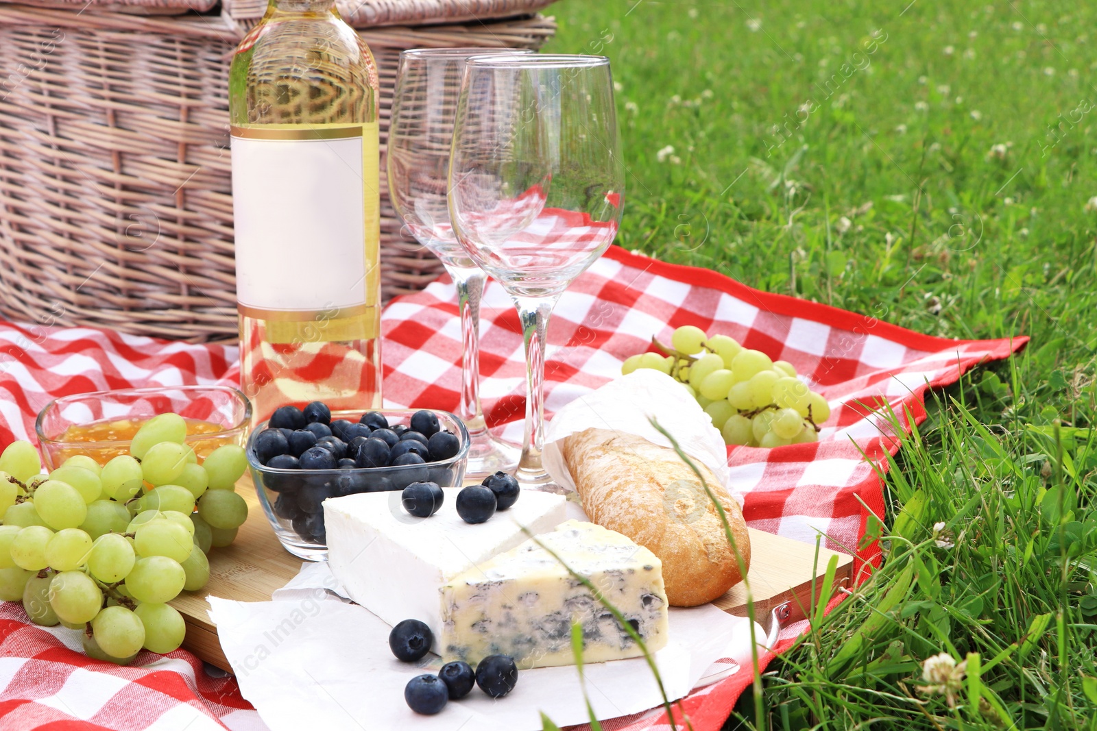 Photo of Picnic blanket with delicious food and wine outdoors on summer day