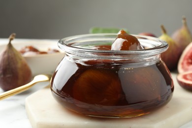 Jar of tasty sweet fig jam on white marble table, closeup