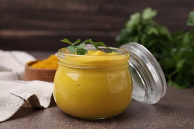 Photo of Jar with tasty curry sauce and parsley on brown table, closeup