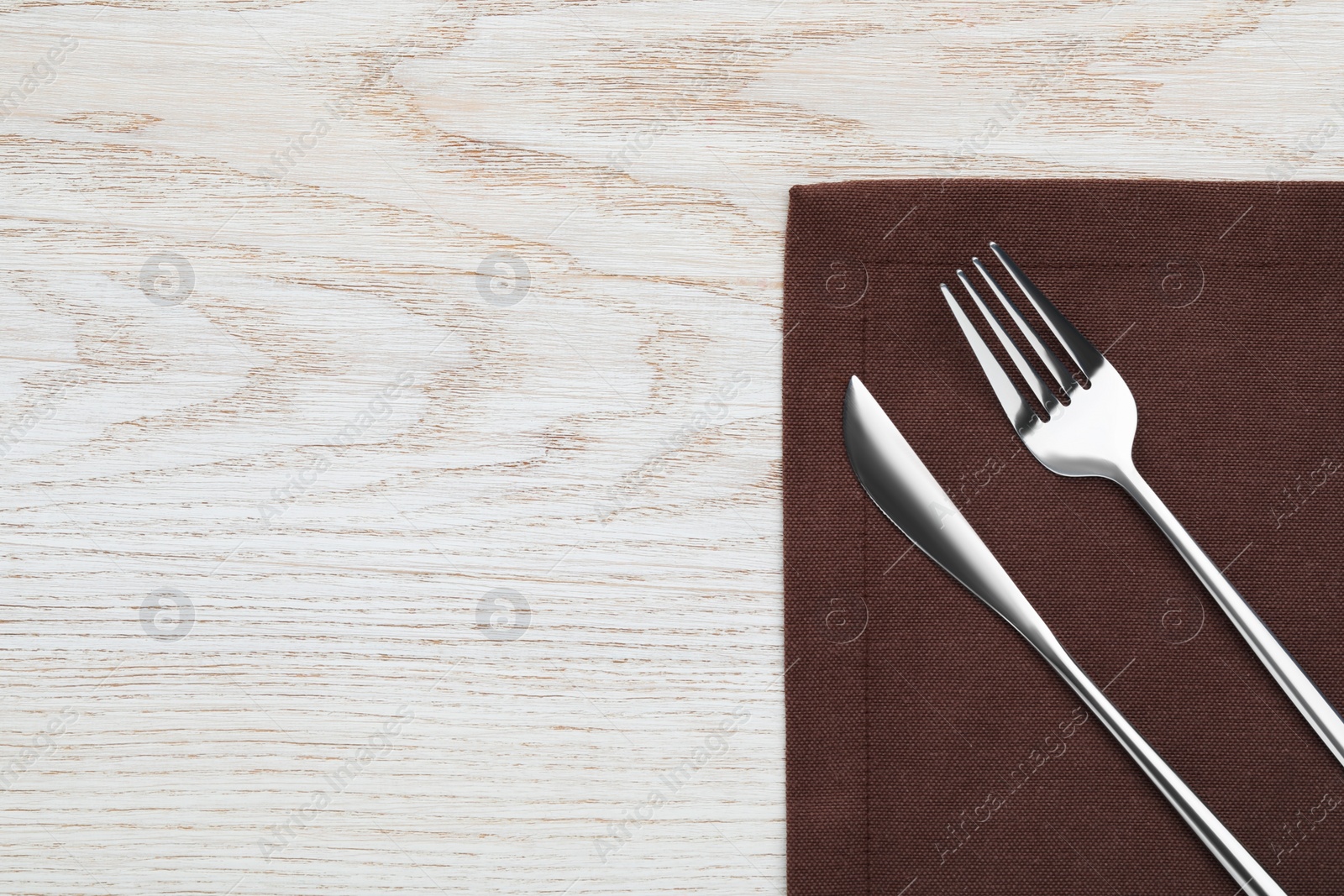 Photo of Fork, knife and napkin on white wooden table, top view with space for text. Stylish shiny cutlery set