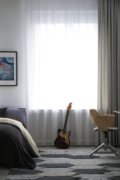 Photo of Modern teenager's room interior with bed and guitar near window