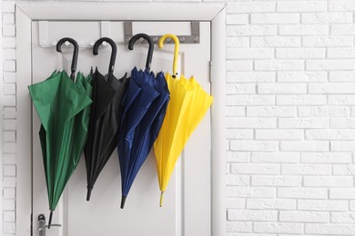 Photo of Closed bright umbrellas hanging on door. Space for text