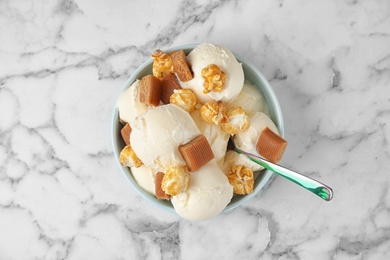 Photo of Plate of delicious ice cream with caramel candies and popcorn on white marble table, top view