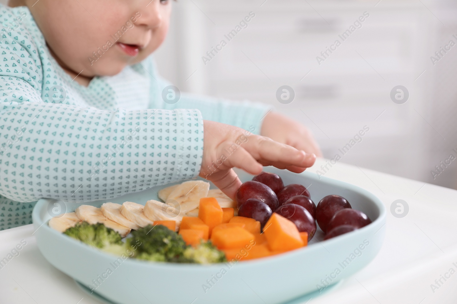 Photo of Little baby eating food from plate at home, closeup