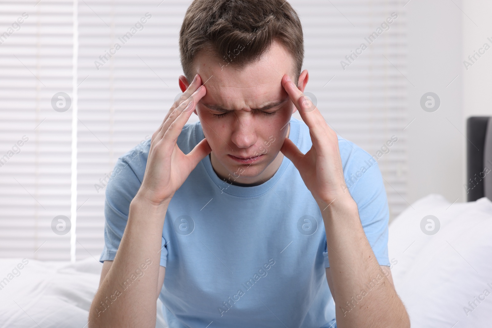 Photo of Sad man suffering from headache on bed indoors