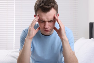 Sad man suffering from headache on bed indoors