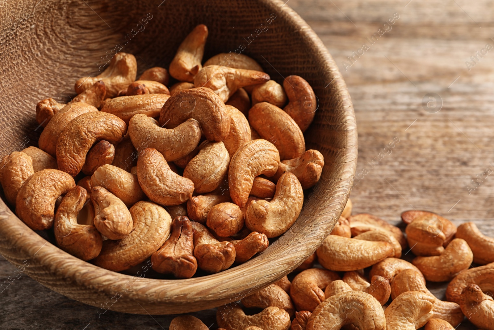 Photo of Tasty cashew nuts scattered from bowl on table, closeup