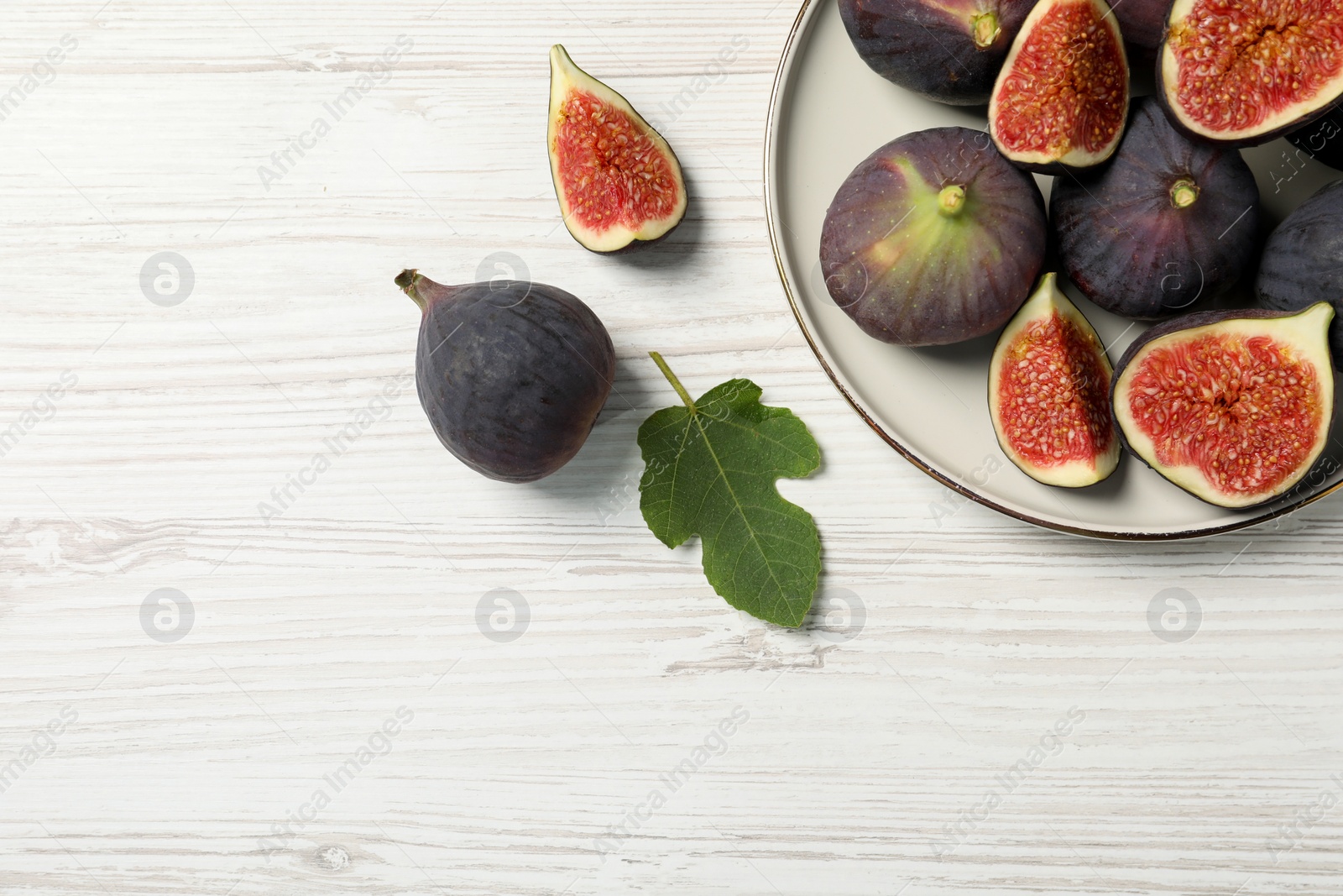 Photo of Whole and cut ripe figs with leaf on white wooden table, flat lay. Space for text