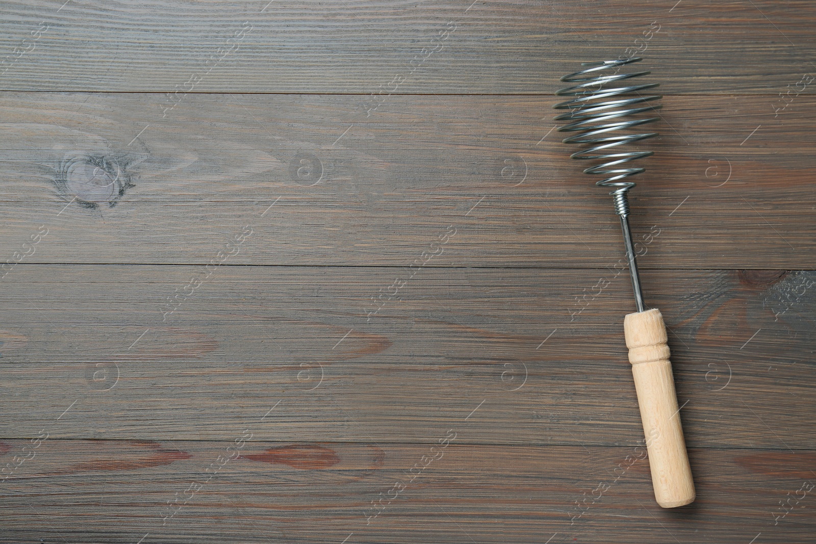 Photo of One metal whisk on wooden table, top view. Space for text