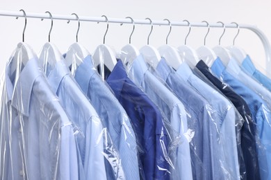 Photo of Dry-cleaning service. Many different clothes in plastic bags hanging on rack against white background, closeup