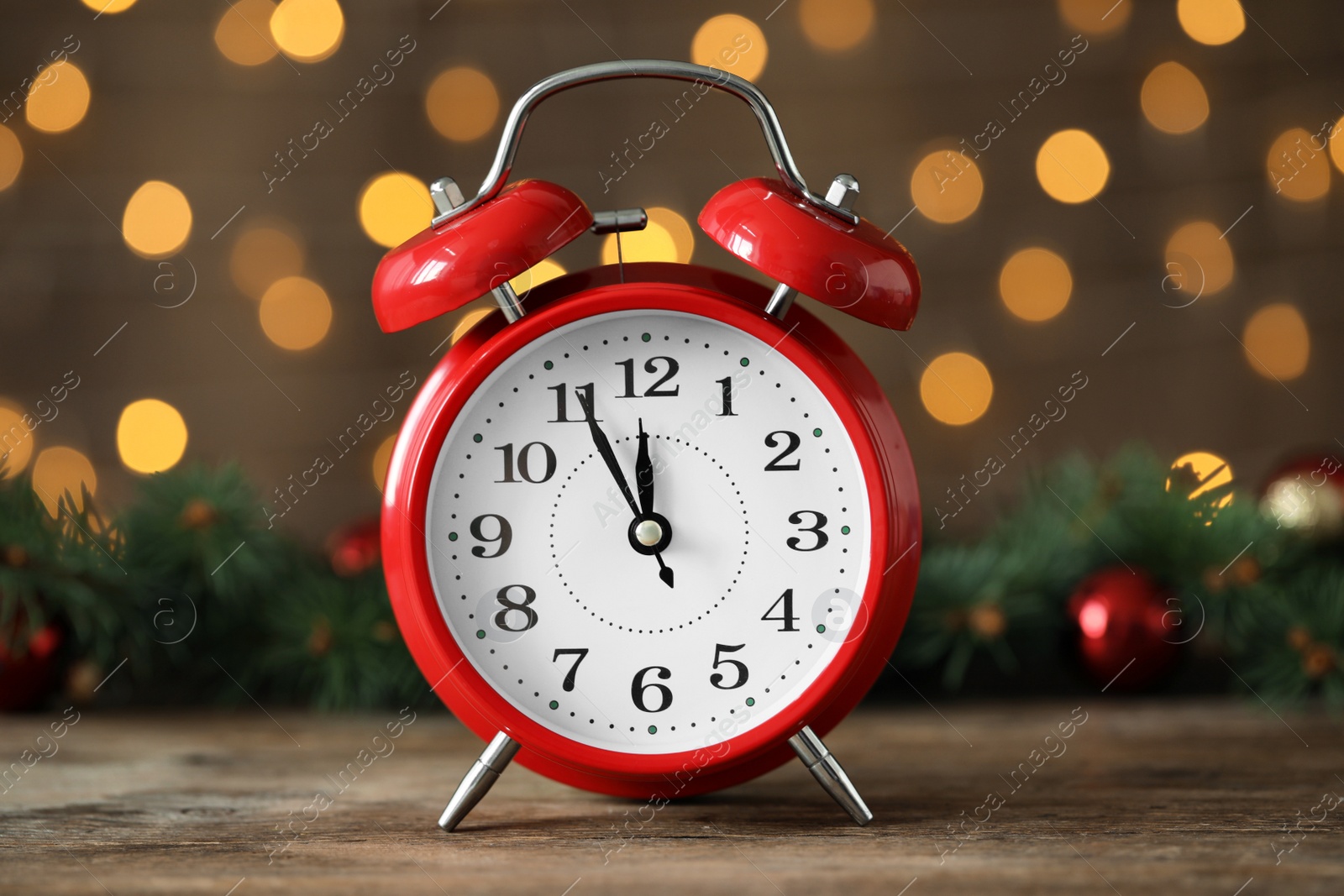 Photo of Alarm clock with decor on wooden table against blurred Christmas lights, closeup. New Year countdown