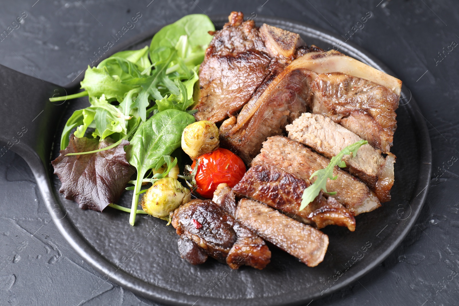 Photo of Delicious grilled beef meat, vegetables and greens on black table, closeup