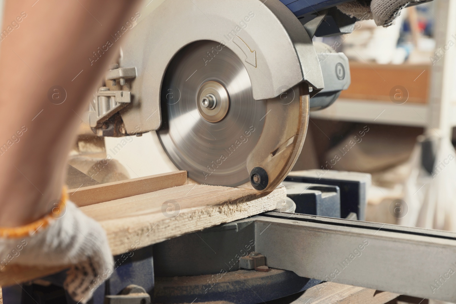 Photo of Professional carpenter cutting wooden planks with sawmill in workshop, closeup