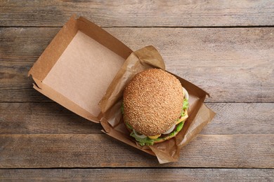 Photo of Delicious burger in cardboard box on wooden table, top view
